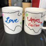 two coffe mugs with an outline of the us. Hearts in the pacific north west and north carolina regions. one says love in the middle of the country the other 'old friends' in french.