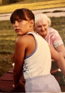 Young girl with dark brown hair looking back over her shoulder. Older woman in the background looking at her.