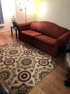 Rust red couch next to coordinating rug, framed by aqua end tables and grey leather recliner