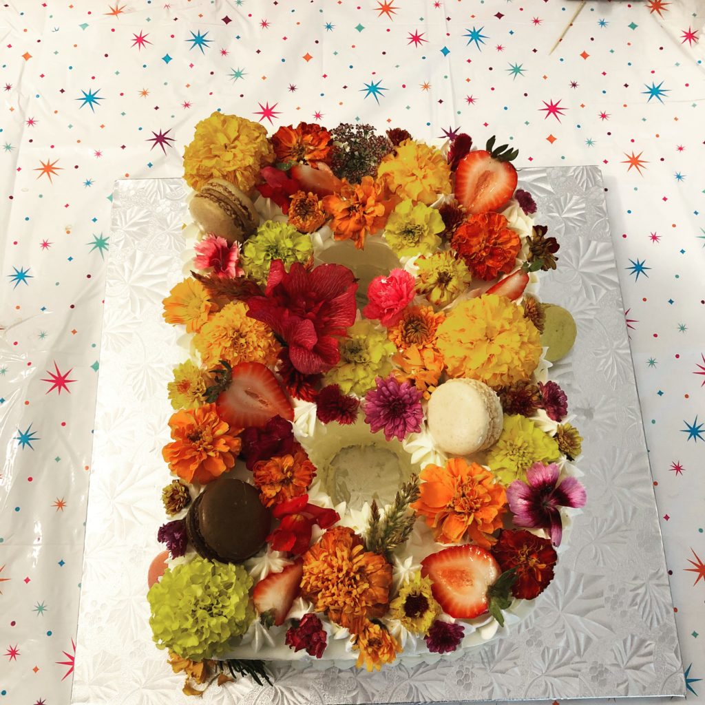 Cake shaped like. Letter B, decorated with edible flowers, strawberries, and macaroons.