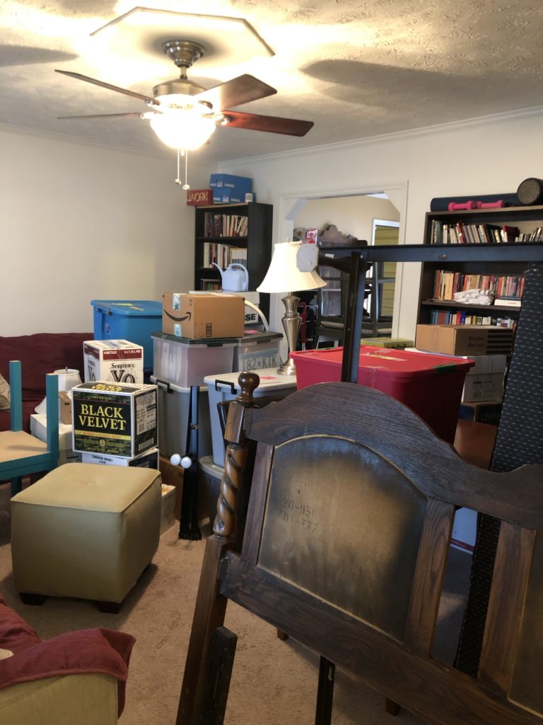 Room filled with the stuff of moving, boxes, a wooden bedframe, mattress, box spring, etc.