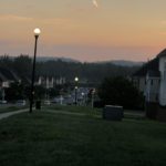 a dark street, looking across a neighborhood to hills with a sky lightening from purple to orange as the sun comes up