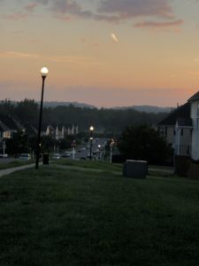 a dark street, looking across a neighborhood to hills with a sky lightening from purple to orange as the sun comes up