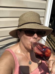 A woman sitting in the sun with sunglasses and straw hat, taking a sip from a fruitfilled glass of sangria.