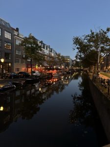 Amsterdam canal at night, dusk. The sky is still a bit blue, but the street and cafe lights are on.
