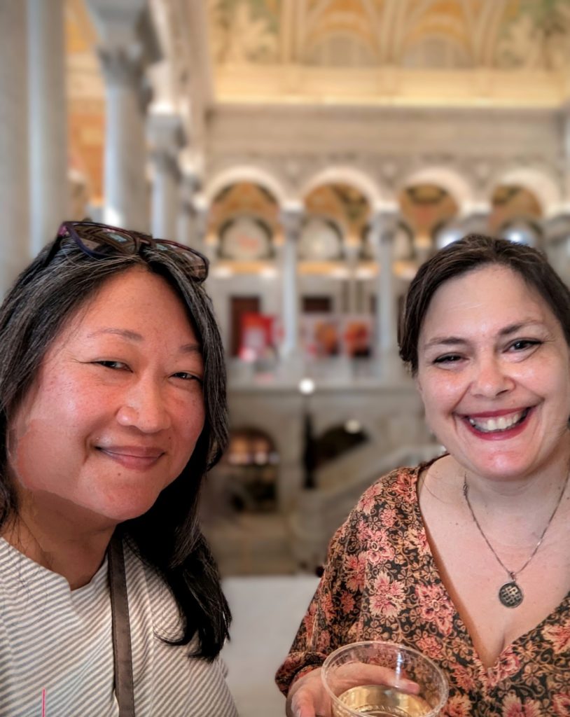 Two women smiling into the camera. They are inside the library of congress, one visibly holds a glass of wine. 