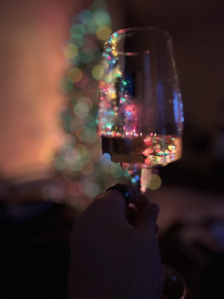 Lit Christmas Tree as seen through a wine glass with white wine. 