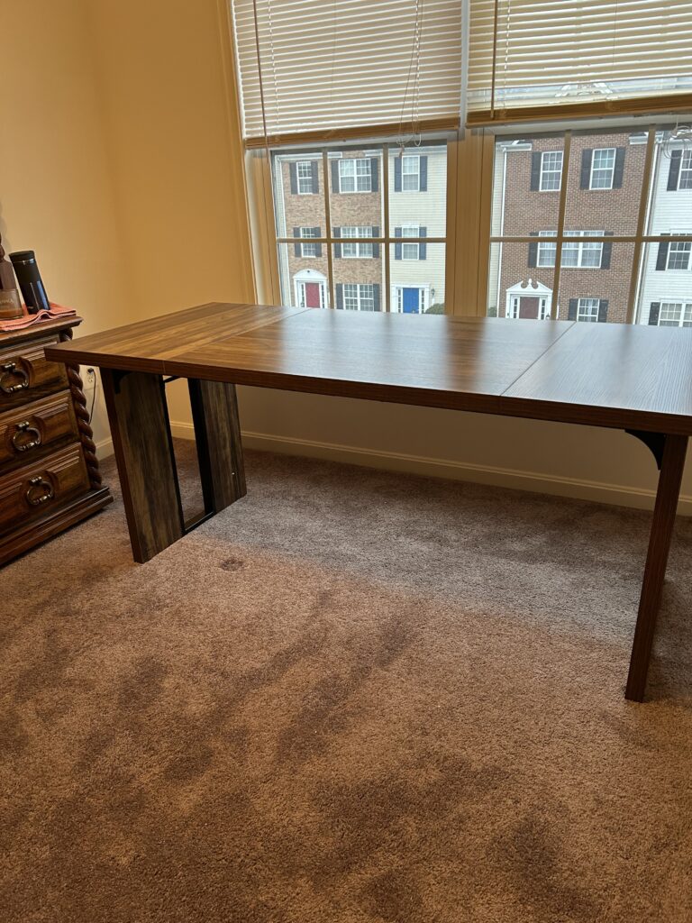 Long, simple, executive desk in front of a double set of windows.