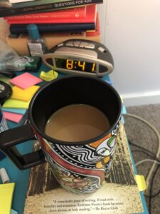 A night stand full of books, an alarm clock, post-it notes, and a cup of coffee.